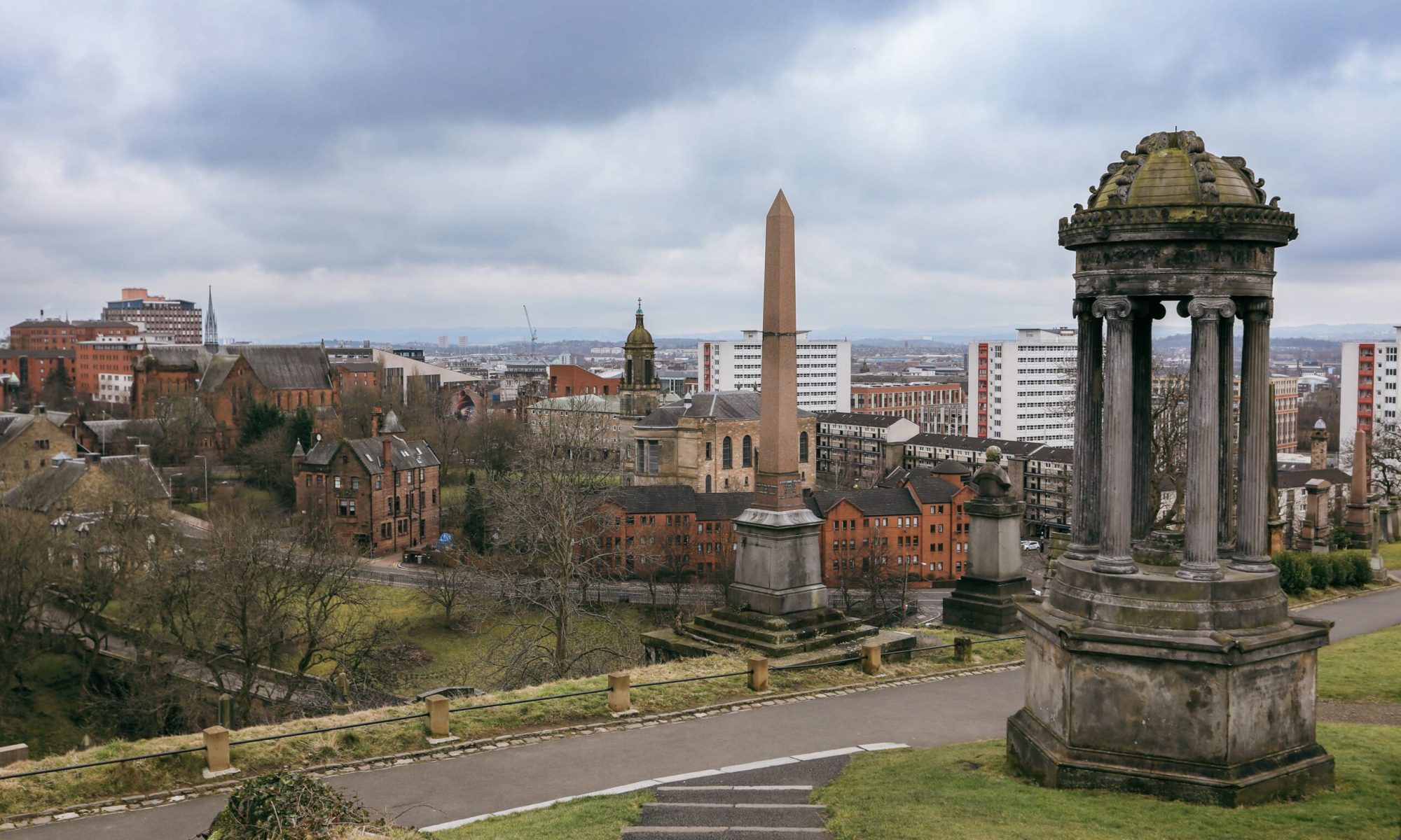 Visitors admire the impressive architecture of Glasgow Cathedral alongside the vibrant city skyline on a cloudy day.